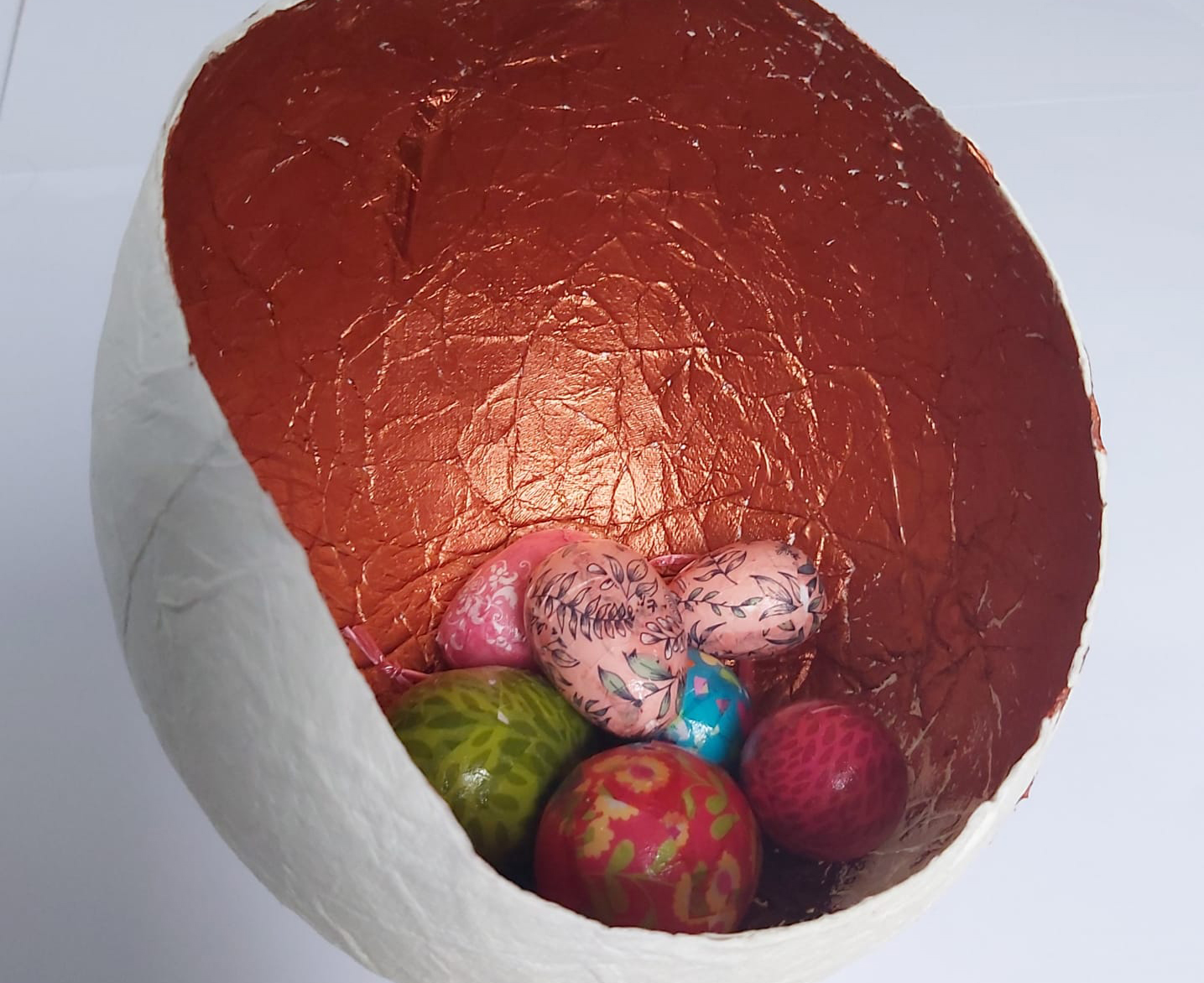 Papier-mache Easter egg with a white exterior and shimmering gold interior. Miniature eggs which are painted with silver and gold patterns are painted on the eggs.