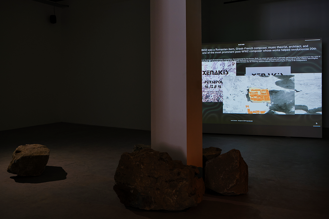 a dark room with a projector, a column and some stones