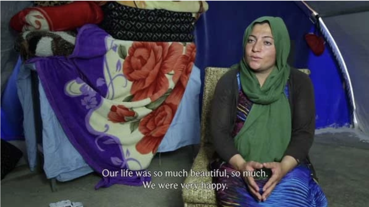 our life so much beautiful, so much. We were very happy. a seated speaking woman with a green veil. behind her is a curtain