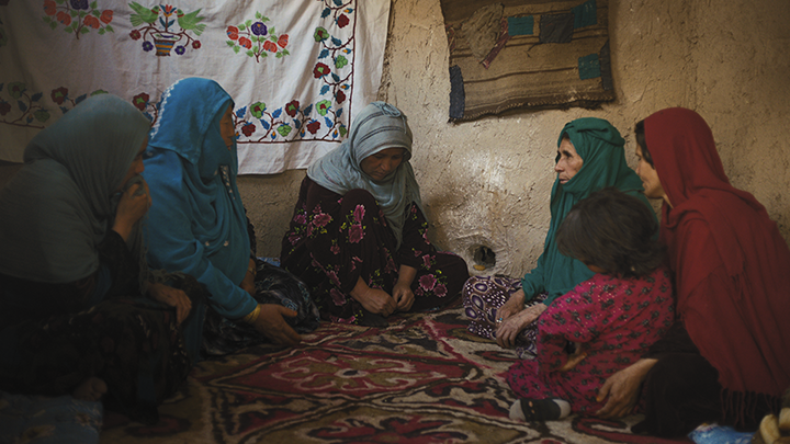 five women and a little girl sitting on the floor of a house, there are sheets hanging on the walls