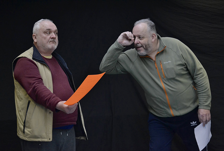 two people acting against a black background