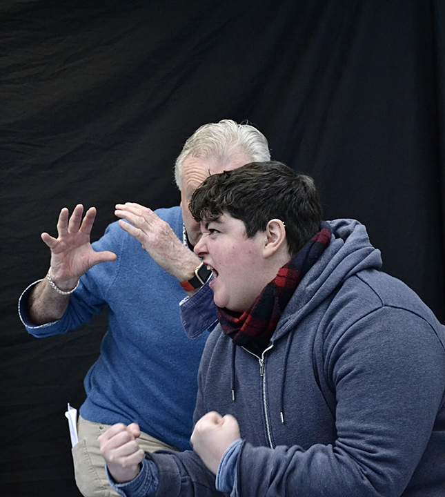 two people posing facing each other, the person in front is turned in profile and covers the one behind, the background is black