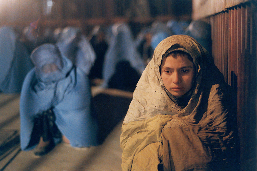 a crying baby with a white blanket leaning against a wall. in the background other people with blue blankets