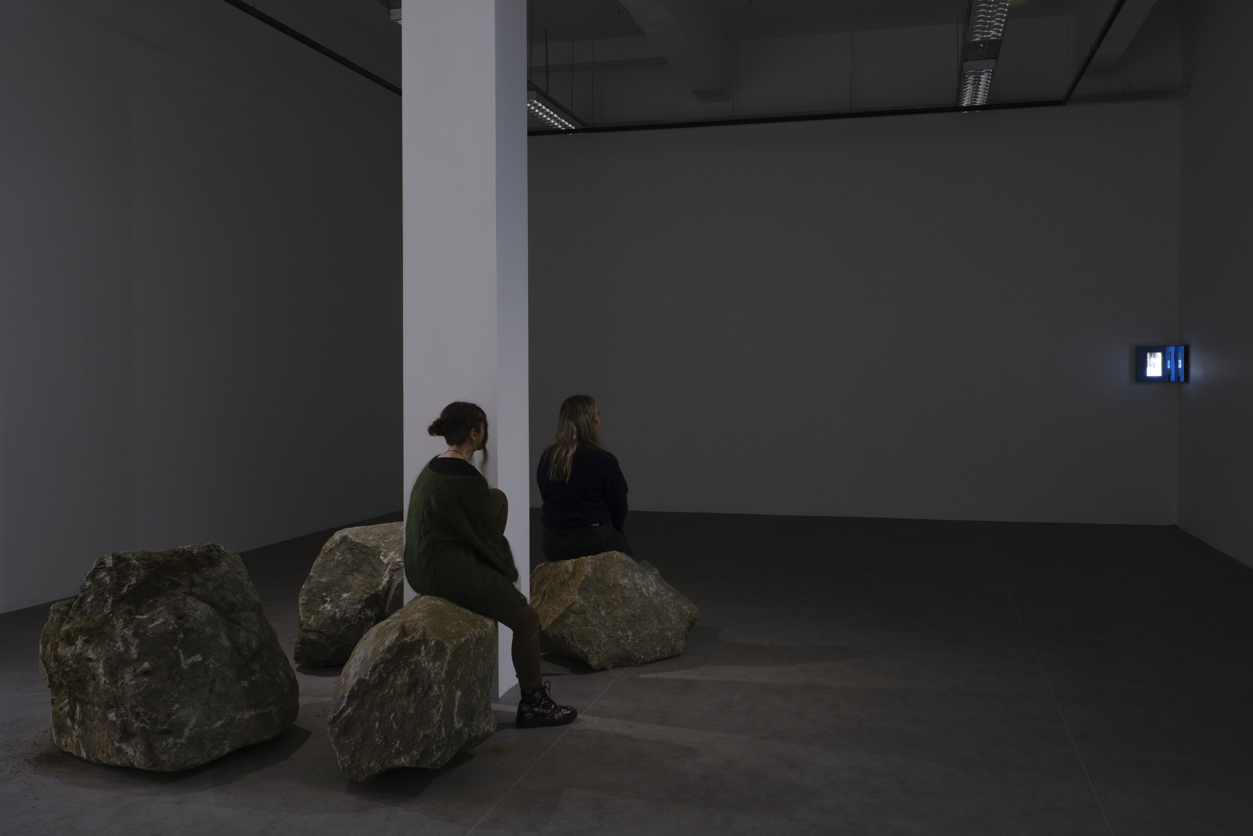two girls sitting on stones at the foot of a white column looking at an opera