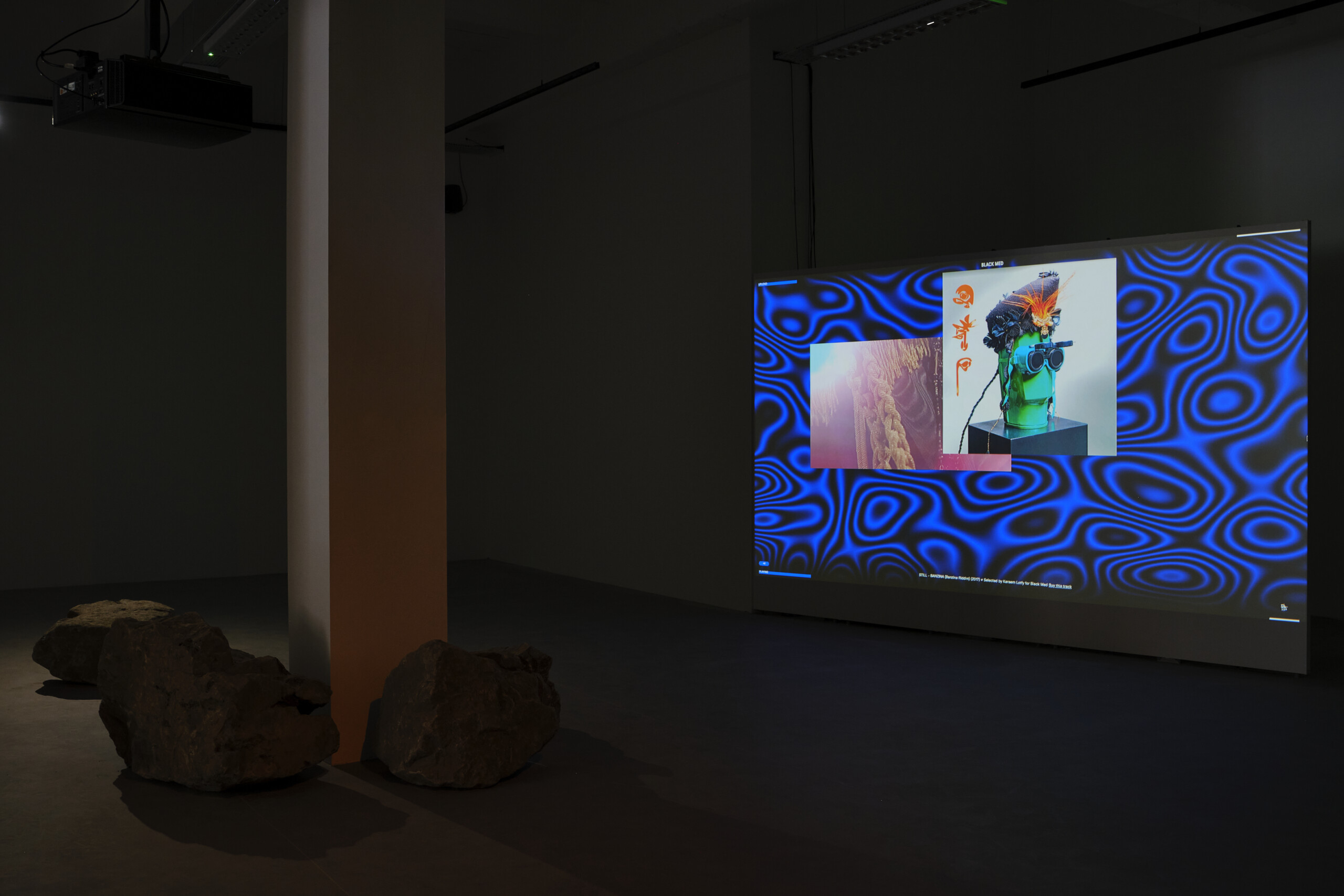 dark room with a column to the left, with stones at its feet. To the right is a large TV