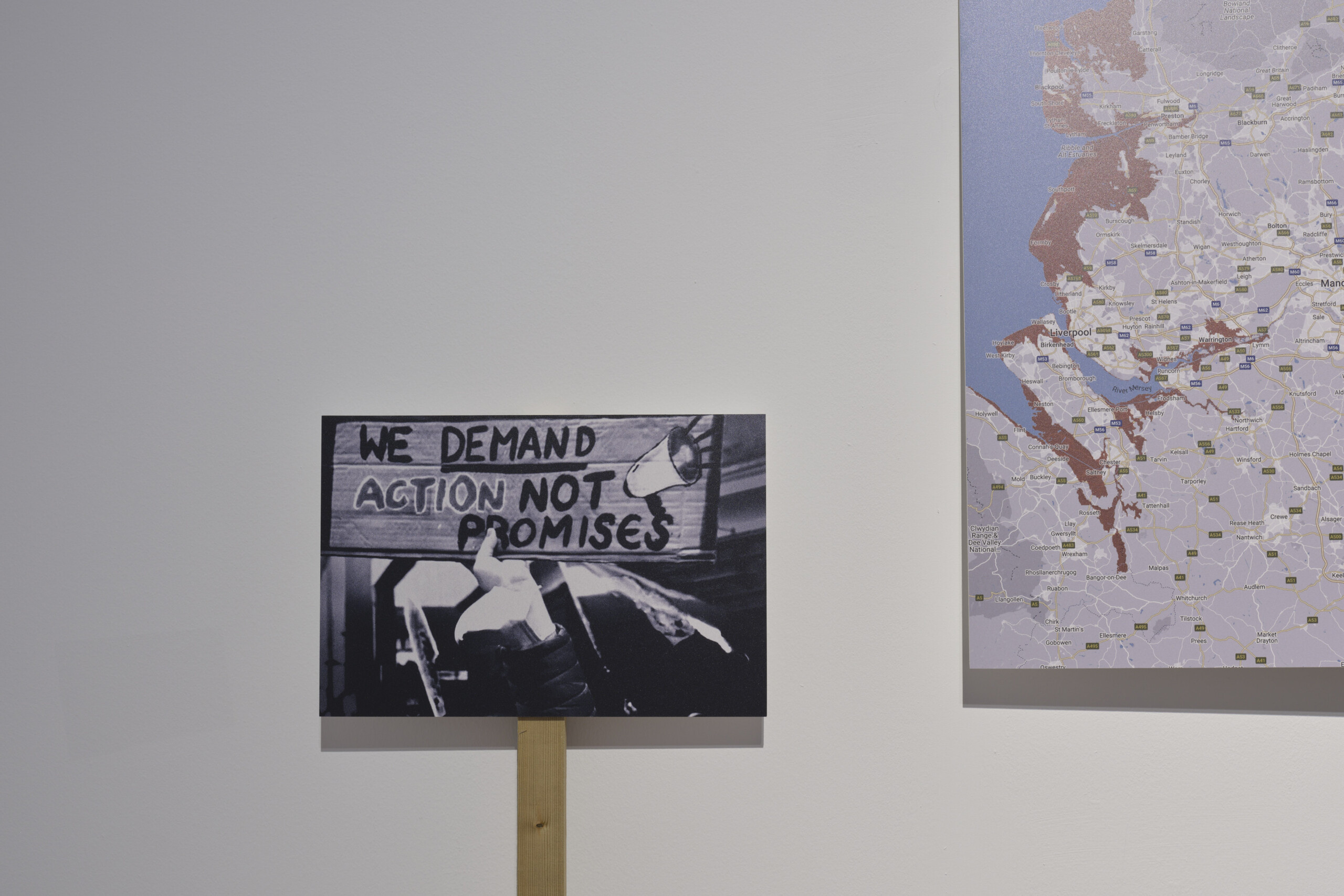 White wall with small placard in black and white of a protest and the corner of a large map in white, brown and blue